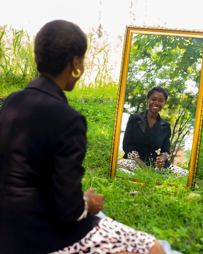 services-01 A woman in a blazer smiles into a mirror placed on grass outside.
